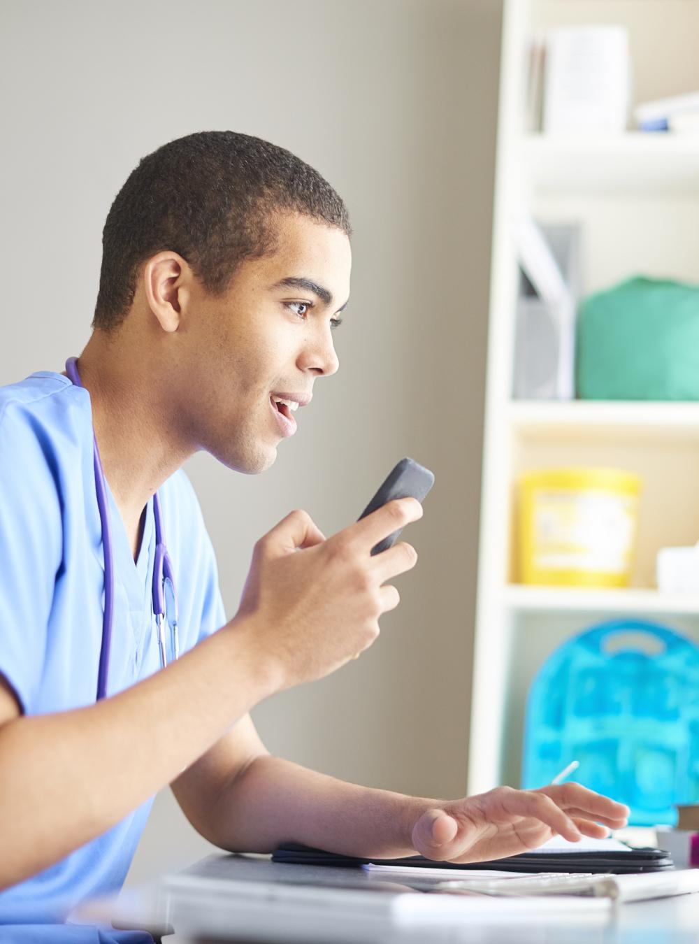 Young doctor at a desk using a speech recognition platform to dictate data directly into electronic health records