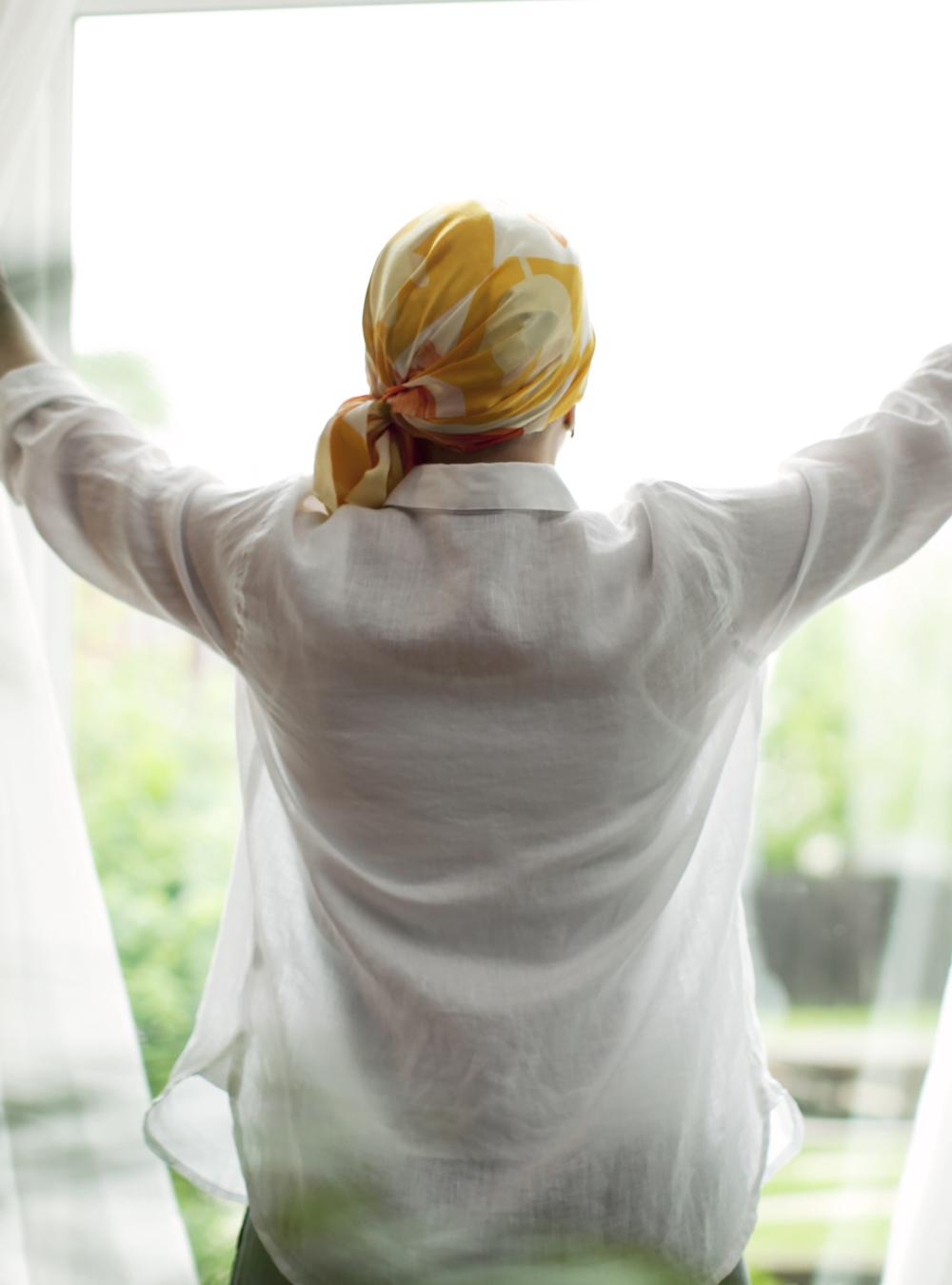 Woman in a headscarf looking out a window into nature, evoking a feeling of wellness