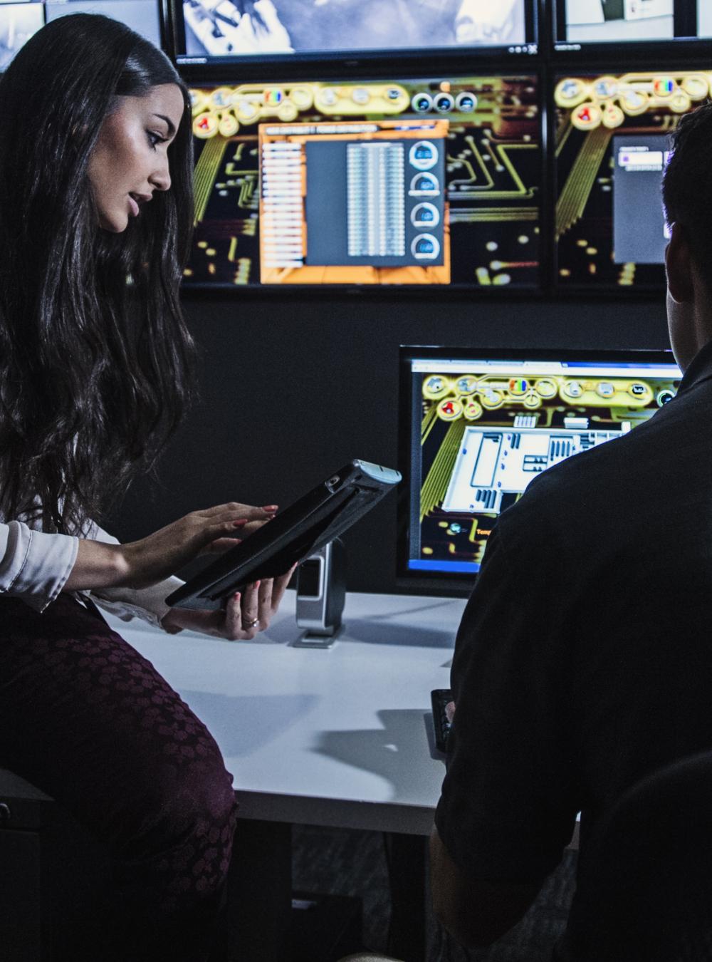 Woman and man in a security control room surrounded by video monitors