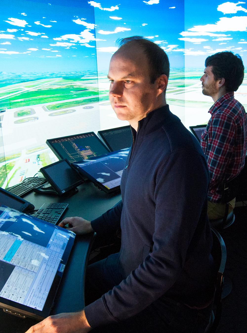 Employees in the IDEA Lab simulator standing in front of a large video display of an airport