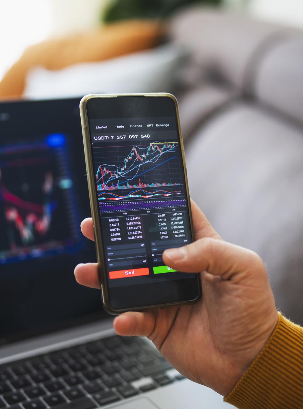 person looking at stock market on mobile phone and laptop