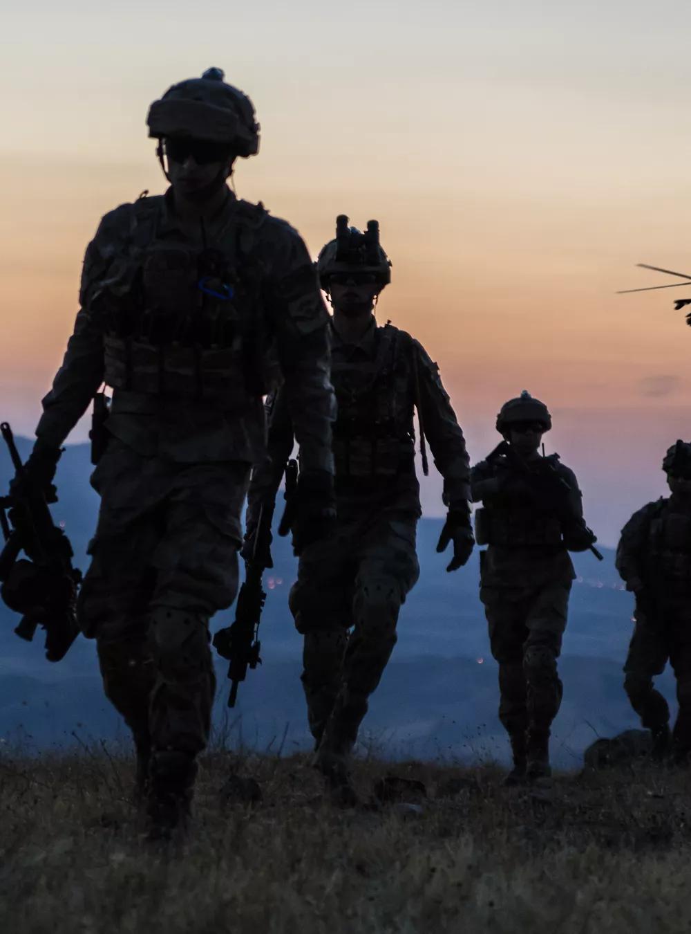 Soldiers walking up a hill at twilight and a helicopter is flying overhead