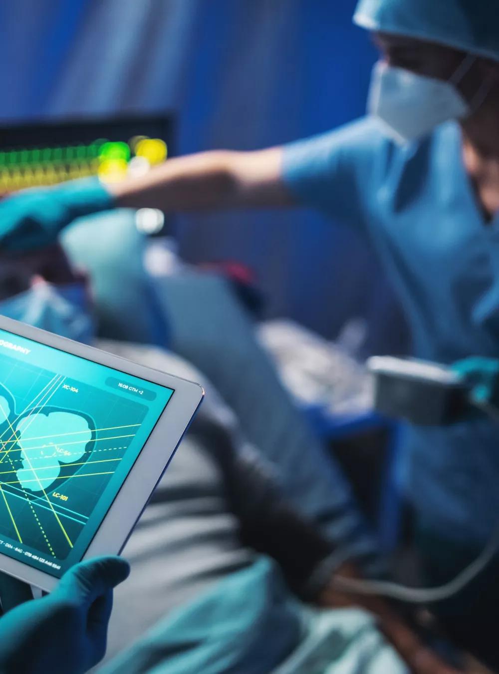 Medical professionals treating a patient in a hospital. One of the doctors is holding a tablet showing a scan of the patient's internal organs