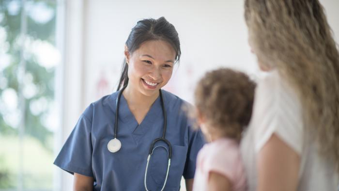 Clinician smiling at a pediatric patient who is accompanied by a caregiver