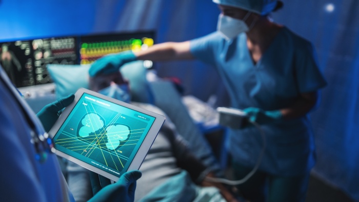 Medical professionals treating a patient in a hospital. One of the doctors is holding a tablet showing a scan of the patient's internal organs